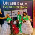 drei Musiker*innen der marchin Band Evas Apfel, die gerade im Shopping center Skyline Plaza in Frankfurt bei einem Auftritt sich zu einem Foto formatieren